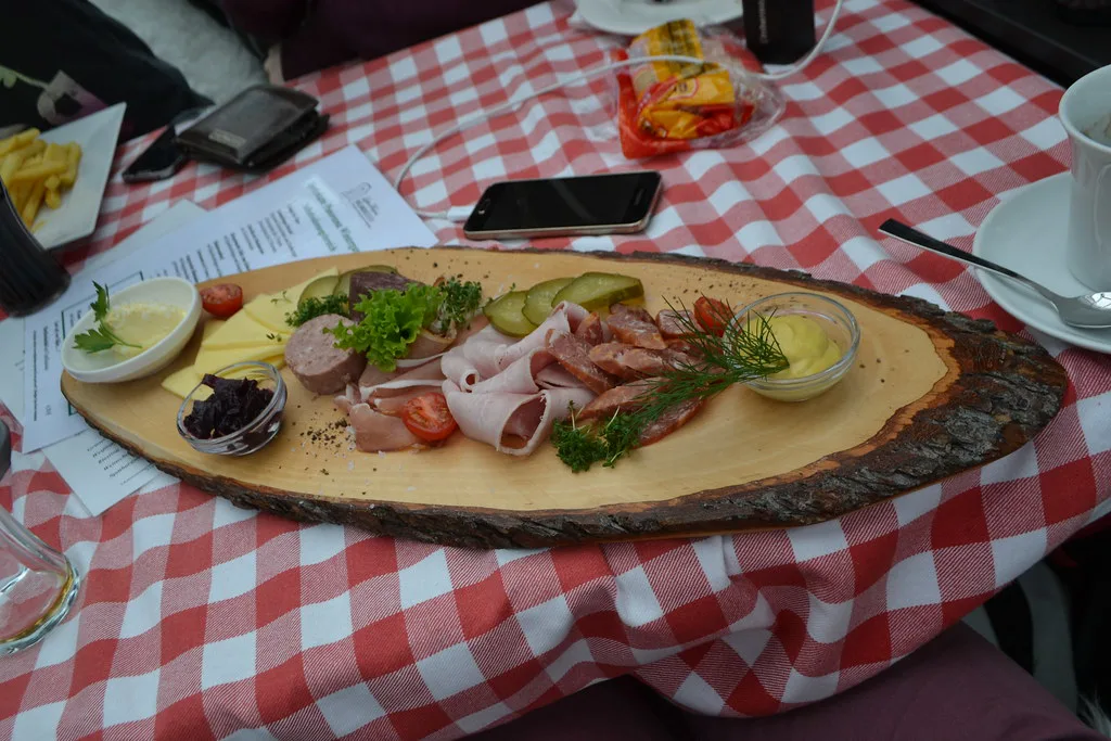 A bread board with cold cuts, cheese and salad on a checked tablecloth at the Restaurant am Rolandsbogen.