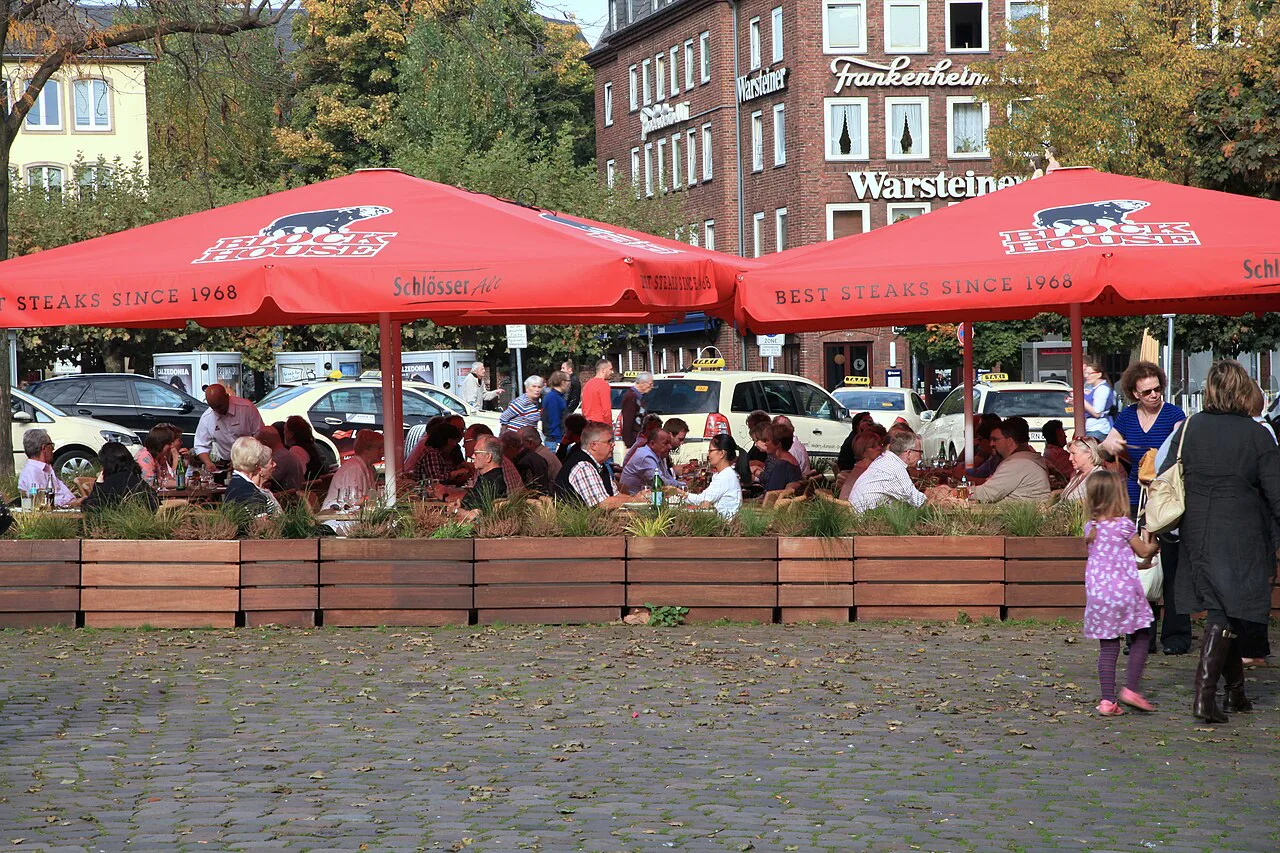 Outdoor café tables under red umbrellas on Burgplatz in the old town, Düsseldorf.