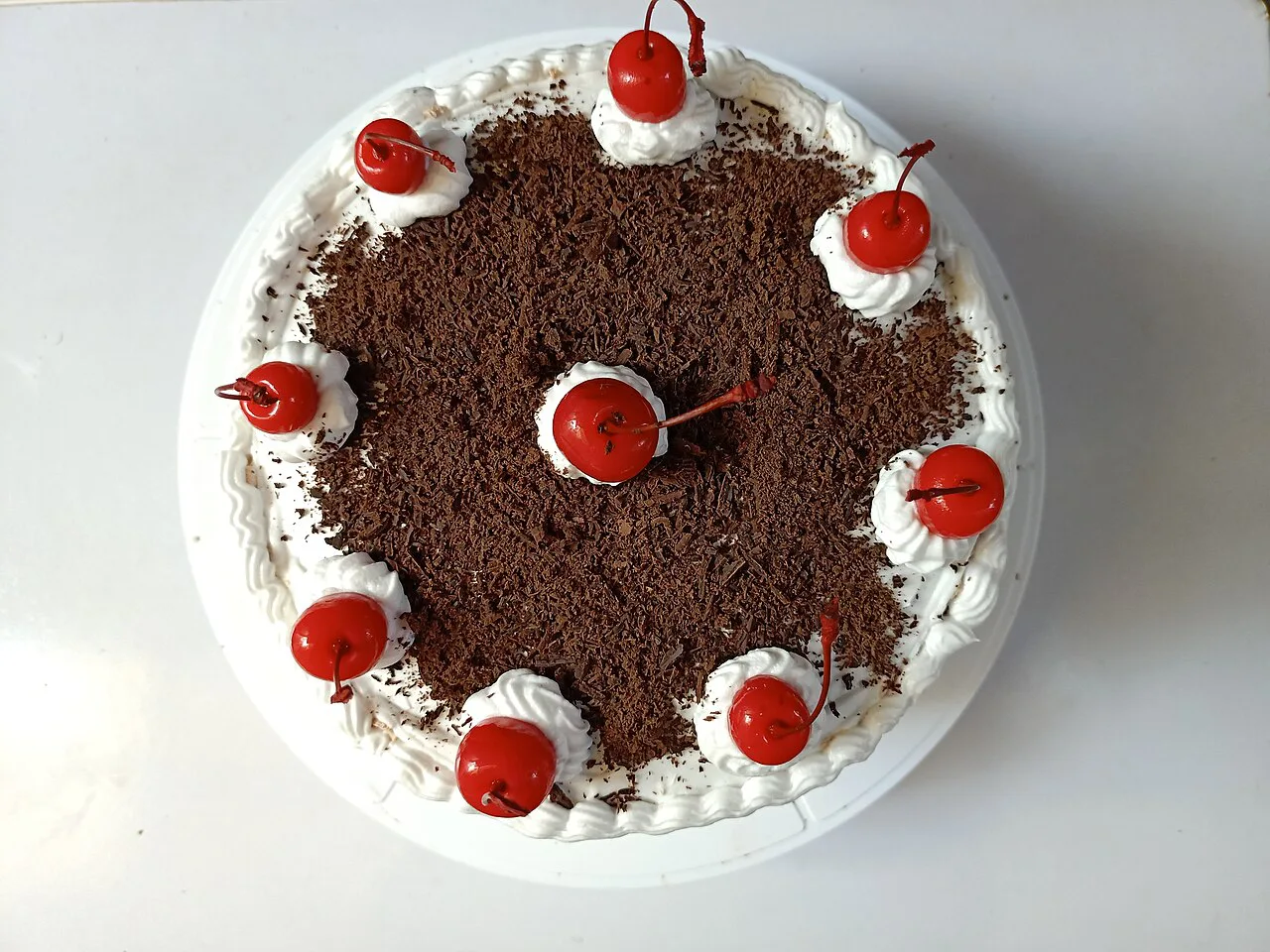 A whole Black Forest cake decorated with cherries and cream.