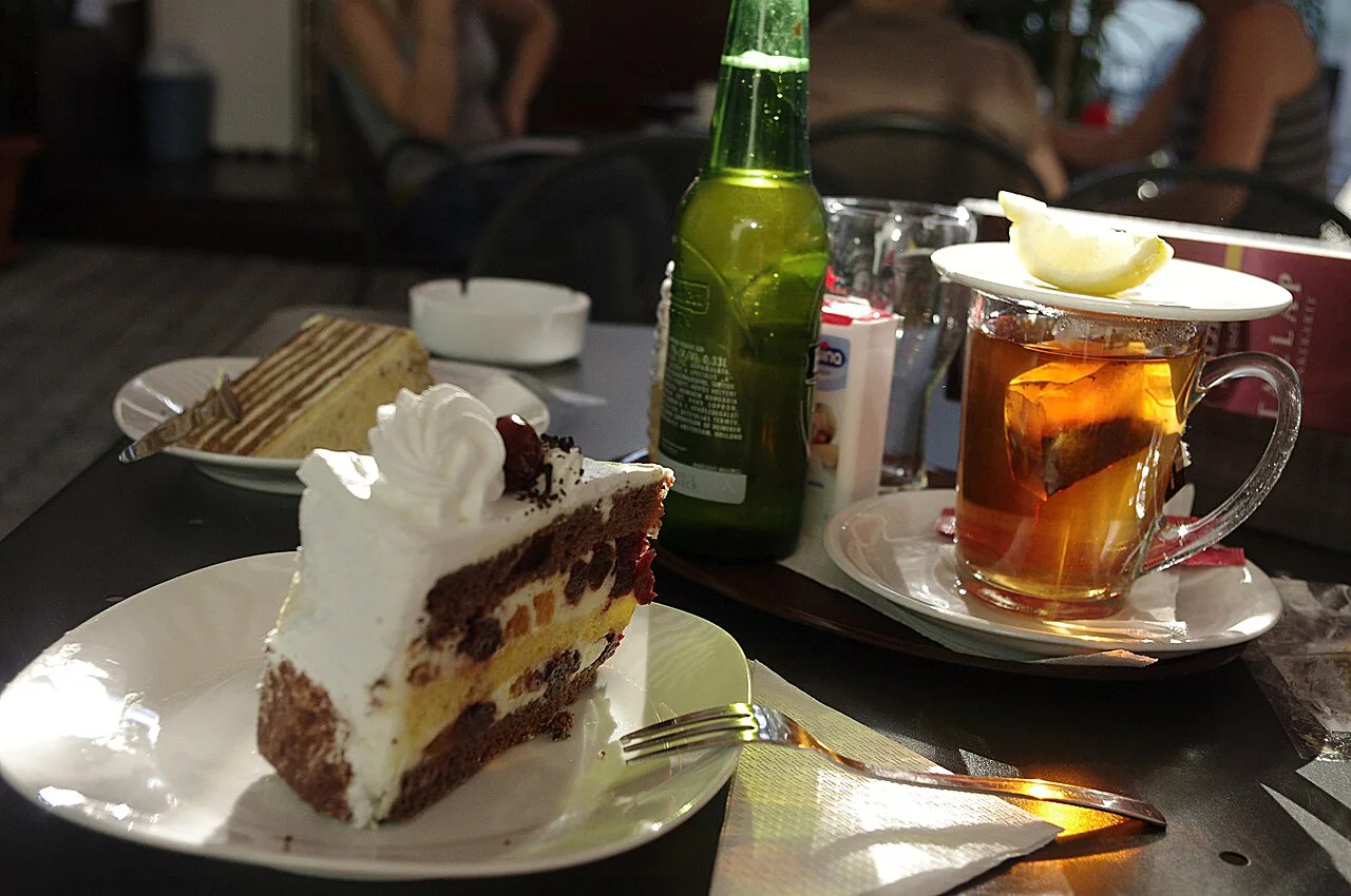 A slice of Black Forest cake served with tea in a pastry shop.