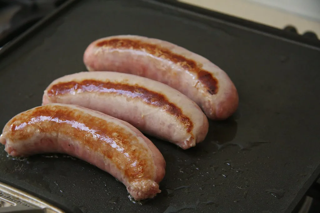 Bratwurst browning in a pan.