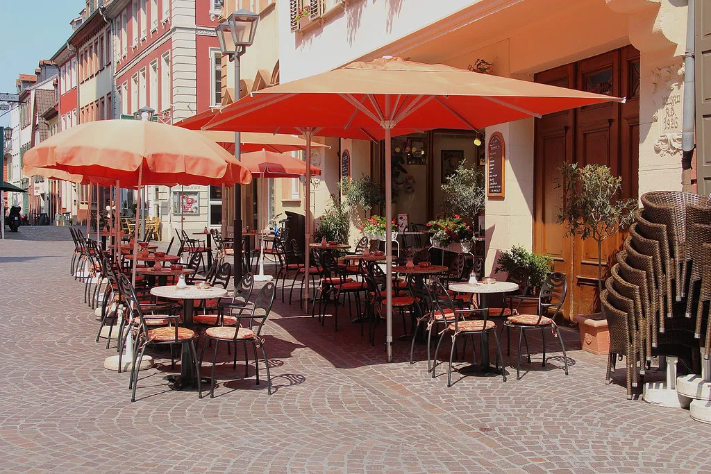 Café tables under red umbrellas on an old-town street, Heidelberg.