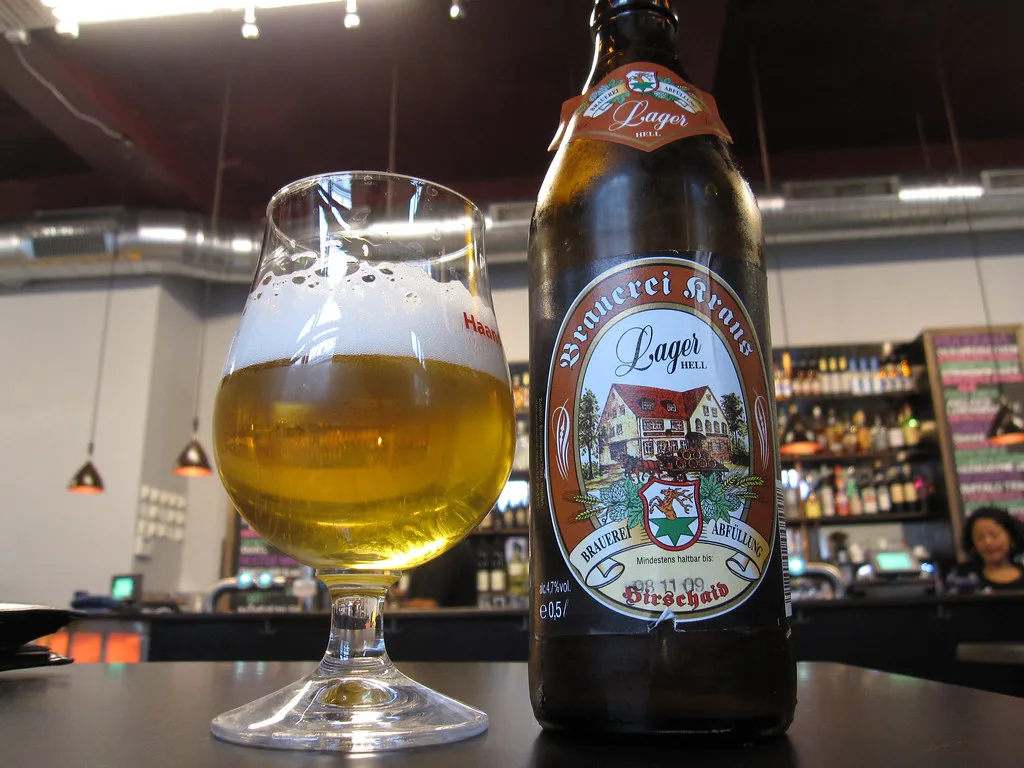 A glass of Brauerei Kraus Lager Hell beside its bottle.
