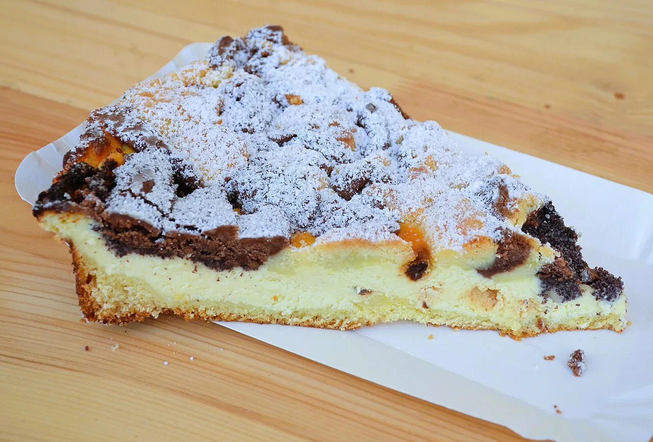 A slice of Käsekuchen with streusel and poppy seeds.