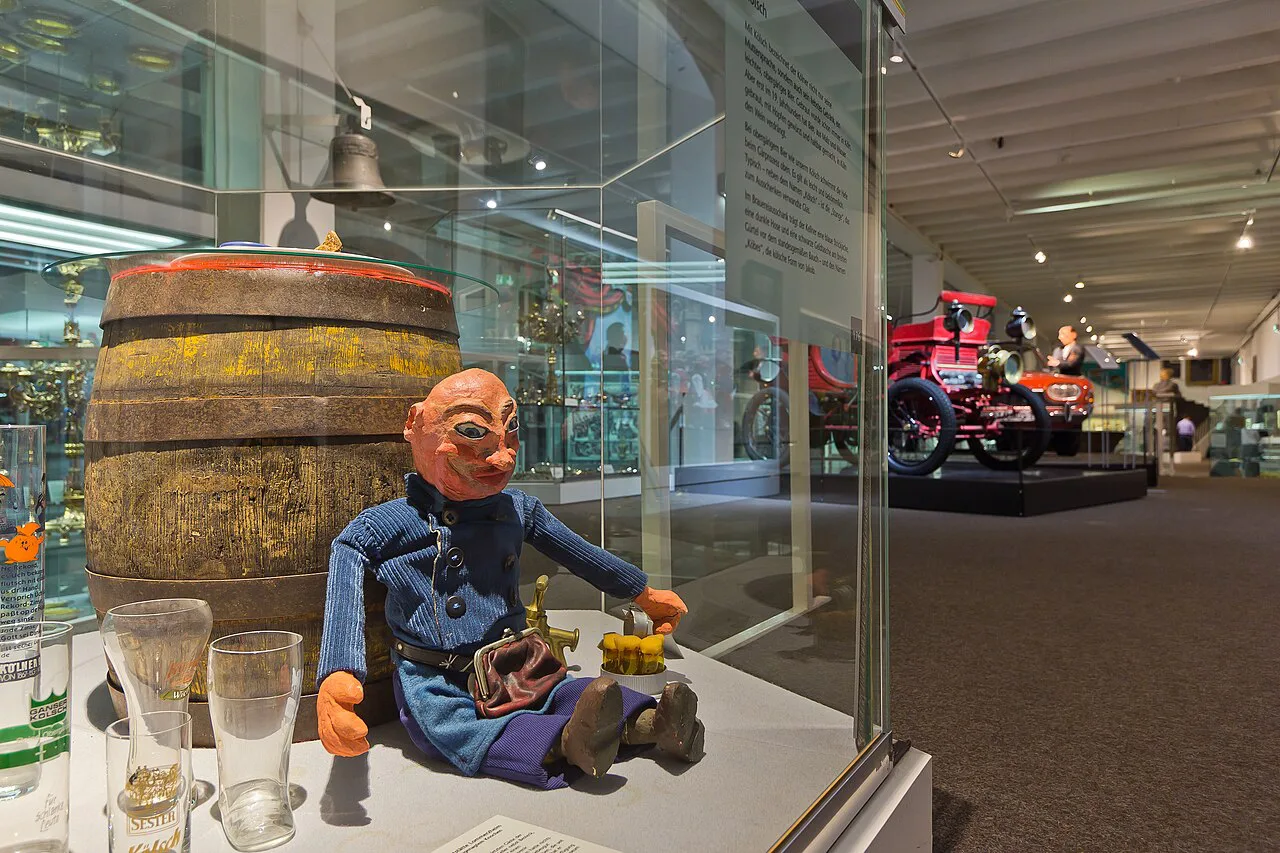 A Köbes figure with a Kölsch barrel and Stange glasses on display at the Cologne City Museum.