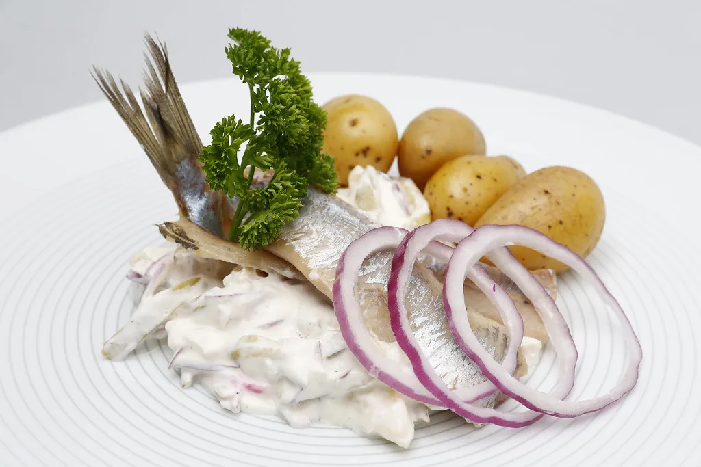 Matjes herring with boiled potatoes, onion rings and a creamy sauce.